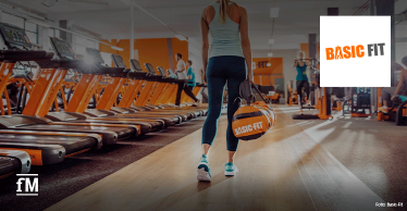 Person mit Sporttasche geht durch einen Fitnessclub mit Laufbändern und Basic-Fit-Logo.