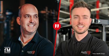 Zwei Männer in schwarzer Arbeitskleidung mit dem Logo ‚BestFit Group‘ posieren lächelnd nebeneinander vor Fitnessgeräte-Kulisse – links ein Mann mit Glatze, rechts ein Mann mit kurzem Haar und Bart.
