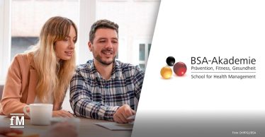 Zwei Personen sitzen an einem Tisch vor einem Fenster und betrachten gemeinsam Dokumente, rechts eine Tasse auf dem Tisch.