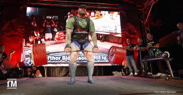 Ein Strongman-Athlet hebt bei einem Wettkampf eine mit vielen roten Gewichtsscheiben beladene Langhantel vom Boden; im Hintergrund jubeln Zuschauer, auf einer großen Leinwand ist der Name 'Hafthor Björnsson' und das Gewicht '505 kg' zu sehen.