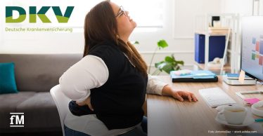 Eine Frau sitzt am Schreibtisch vor einem Computer, lehnt sich mit schmerzverzerrtem Gesicht zurück und hält sich den unteren Rücken. Links oben ist das DKV-Logo zu sehen.