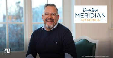 Ein lächelnder Mann mit Brille und grauem Bart sitzt in einem hellen Raum vor einem Fenster. Es handelt sich um Marcel Kloos, den neuen Country Director von David Lloyd Clubs Deutschland.