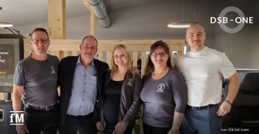 Fünf Personen stehen lächelnd nebeneinander in einem modern eingerichteten Therapieraum der Physiopraxis Hermes. Drei tragen Kleidung mit dem Logo 'Hermes Physio Point', eine Person trägt ein weißes T-Shirt, eine weitere Person (Jürgen Adams, 2. von links) trägt Anzugjacke.