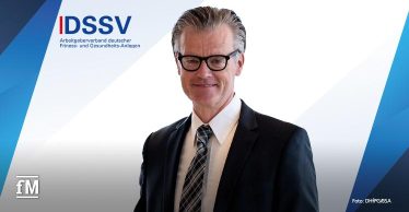 Ein Mann im Anzug und mit Brille steht vor einem Hintergrund mit blau-weißem Design. Links oben steht das Logo des 'DSSV'.