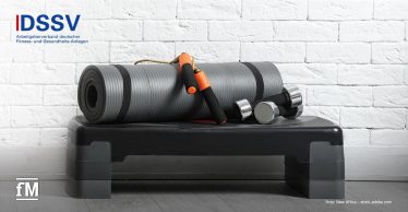 Graue Trainingsmatte, Kurzhanteln und Springseil auf einem Steppbrett, vor weißer Ziegelwand, links oben DSSV-Logo.