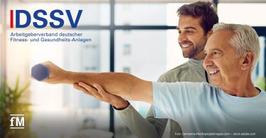 Ein Trainer unterstützt einen älteren Mann bei einer Armübung mit einer kleinen Hantel. Oben rechts ist das Logo des DSSV in Blau. Unten links das fM-Signet in Weiß.
