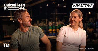 Mann und Frau sitzen lächelnd in einem Fitnessstudio, darüber die Schriftzüge „United let's move.“ und „#BEACTIVE“.