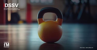 Gelbe Kettlebell mit schwarzem Griff auf Studioboden, im Hintergrund unscharfe Trainingsgeräte und Lichtreflexe.