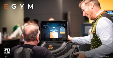 Ein Mann sitzt an einem EGYM-Gerät mit großem Bildschirm, ein weiterer Mann erklärt die Anzeige.