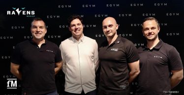 Vier Männer stehen nebeneinander vor einer schwarzen Wand mit EGYM-Logos, zwei tragen EGYM-Shirts, einer Munich Ravens-Kleidung