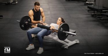 Trainer begleitet eine Sportlerin bei Hip Thrusts im Fitnessstudio und unterstützt sie während der Übungsausführung