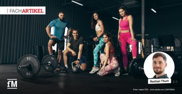 Fünf junge Erwachsene in Sportkleidung stehen und knien mit Hanteln in einem Fitnessstudio