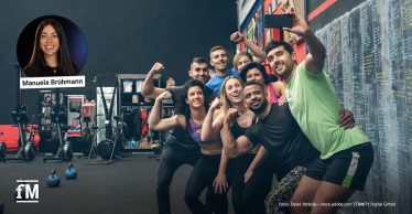 Acht Personen in Sportkleidung posieren gemeinsam vor einer Tafel in einem Fitnessstudio.