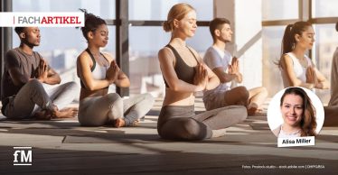 Mehrere Personen sitzen auf Yogamatten in einem hellen Raum und halten die Hände vor der Brust