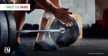 Person beugt sich im Fitnessstudio zu einer Langhantel mit Gewichtsscheiben, klatscht die Hände mit Chalk ein, Staub ist sichtbar in der Luft.