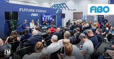 Podiumsdiskussion auf der FIBO: Fünf Personen sitzen auf einer Bühne vor einer großen blauen Wand mit der Aufschrift „Future Forum FIBO“, davor ein dicht besetztes Publikum in Reihen. Im Hintergrund ist ein Bildschirm mit Präsentationsfolie zu sehen, rechts oben das FIBO-Logo.