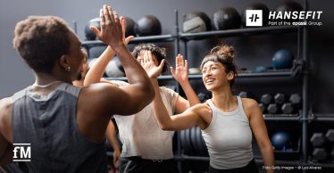 Gruppe von drei Personen im Fitnessstudio klatscht sich lachend beim Training ab.
