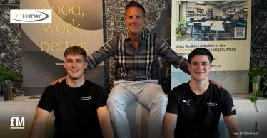 Drei Männer sitzen in einem Innenraum vor einer Wand mit großem Schriftzug „good, work better.“ im linken Hintergrund, einem FITCOMPANY-Logo oben links, einem fM-Logo unten links, einem Fotovermerk „Foto: FITCOMPANY“ unten rechts und einem Plakat mit Büroraum, QR-Code und Texten zu flexiblem Arbeiten rechts im Hintergrund.