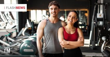 Zwei lächelnde junge Erwachsene in Sportkleidung stehen in einem Fitnessstudio vor Trainingsgeräten; links oben eingeblendet steht „FLASH NEWS“.