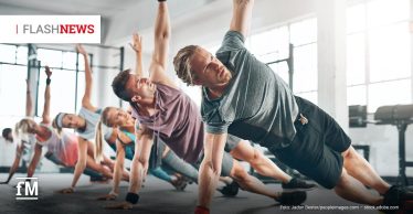 Gruppe von fünf Menschen beim Fitnesskurs im hellen Studio, alle in seitlicher Plank-Position mit ausgestrecktem Arm. Im Vordergrund ein blondhaariger Mann in grauem Shirt und schwarzer Sporthose. Oben links steht „FLASH NEWS“.