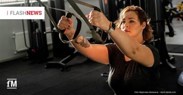 Eine Frau trainiert in einem Fitnessstudio mit Schlingentrainern. Im Hintergrund sind Krafttrainingsgeräte zu sehen.
