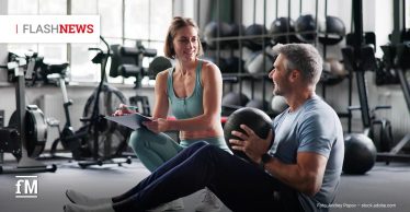 Trainerin berät einen Trainierenden im Fitnessstudio während einer Übung mit einem Medizinball.