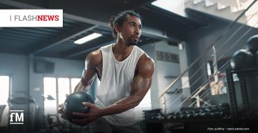 Fitnesssportler mit Medizinball in einem Fitnessstudio, darüber das Logo „FLASHNEWS“