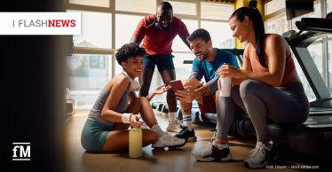 Vier Personen in Sportkleidung sitzen und stehen gemeinsam in einem Fitnessstudio