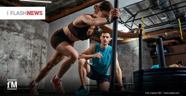 Eine Frau schiebt einen Gewichtsschlitten im Fitnessstudio, während ein Trainer neben ihr kniet.