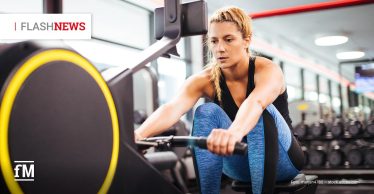 Eine sportliche Frau trainiert konzentriert auf einem Technogym Rudergerät in einem modernen Fitnessstudio. Sie trägt blaue Leggings und ein schwarzes Top. Links oben die Rubrik 'Flashnews' in Großbuchstaben, erstes Wort grau, zweites Wort rot.