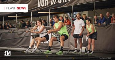 Bei einem HYROX-Fitnesswettkampf ziehen vier Personen gemeinsam an einem dicken Seil, während Zuschauer hinter einer Absperrung zuschauen.