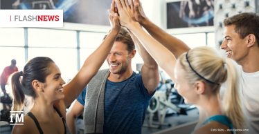 Vier junge Erwachsene in einem Fitnessstudio klatschen lächelnd mit erhobenen Händen ab; im Hintergrund Trainingsgeräte. Oben links steht „FLASHNEWS“, unten links das fM-Logo.