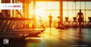 Mehrere Laufbänder in einem Fitnessstudio bei Sonnenaufgang mit trainierenden Personen im Hintergrund.