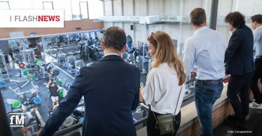 Mehrere Personen blicken von einer Galerie auf ein modernes Fitnessstudio mit Kraft- und Ausdauergeräten; die Szene zeigt eine Führung während einer Fachveranstaltung, dem 14. ALF in Barcelona.