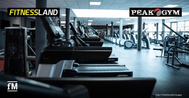 Reihe von Laufbändern und Cardiogeräten in einem hellen Fitnessstudio mit Säulen und großen Fensterflächen.