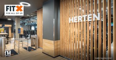 Eingangsbereich des neuen FitX-Studios in Herten mit modernen Holzelementen und Trainingsgeräten im Hintergrund.