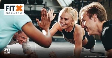 Frau trainiert in einem FitX-Studio mit einer Langhantel über dem Kopf
