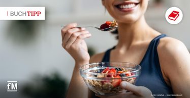 Frau isst lächelnd Müsli und frische Beeren aus einer Schale.