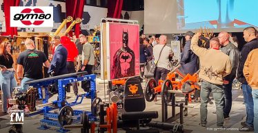 Menschen betrachten Fitnessgeräte und Kunstwerke in einer großen Halle mit roten Vorhängen.