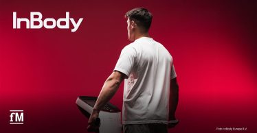 Ein sportlich gebauter Mann steht in weißem Shirt auf einem InBody-Messgerät und blickt in einen kräftig roten Hintergrund. Links oben das InBody-Logo, unten links das fM-Logo.