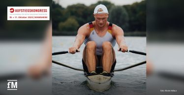 Ein Ruderer in Sportkleidung sitzt im Einer-Boot und rudert auf einem ruhigen Gewässer. Er trägt eine Kappe und schaut konzentriert nach vorn. Links oben im Bild befindet sich das Aufstiegskongresslogo.