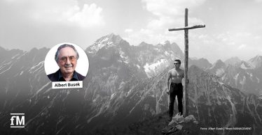 Schwarz-Weiß-Aufnahme eines Mannes neben einem Gipfelkreuz in den Bergen, ergänzt um ein rundes Porträt von Albert Busek.