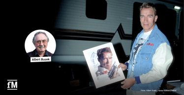 Arnold Schwarzenegger hält ein Filmplakat zu 'True Lies'; links im Bild ein Porträtfoto von Albert Busek mit Namensbeschriftung.