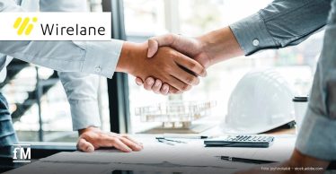 Zwei Personen im Business-Outfit geben sich die Hand über einem Tisch mit Dokumenten, Tablet, Taschenrechner, Kaffeebecher. Oben links befindet sich das Logo des Ladeinfrastruktur-Anbieters Wirelane.