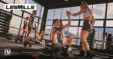 In einem Fitnessstudio trainieren mehrere Personen gemeinsam mit Step-Plattformen und Hanteln.