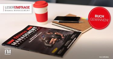Die Zeitschrift fitness MANAGEMENT international liegt auf einem Tisch, daneben steht ein rot-weißer Trinkbecher, rechts liegt ein Heft mit Kugelschreiber und Handy