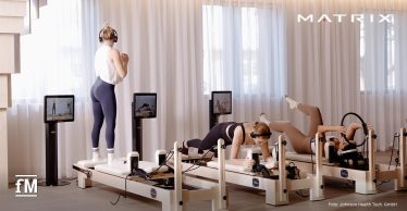 In einem hellen Studio trainieren drei Personen auf Reformer-Geräten mit Monitoren und Kopfhörern