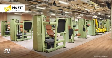 Bereich mit mehreren grünen Kraftmaschinen und braunen Polstern auf hellem Boden im McFIT Berlin-Prenzlauer Berg.