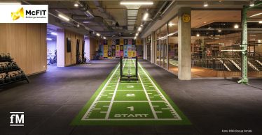 Moderner McFIT-Trainingsbereich mit grünem Indoor-Sprinttrack, Gewichtsschlitten und offener Fläche für funktionelles Training