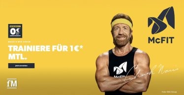 Chuck Norris steht vor gelbem Hintergrund, trägt schwarzes McFIT-Shirt und gelbes Stirnband und verschränkt die Arme vor der Brust.